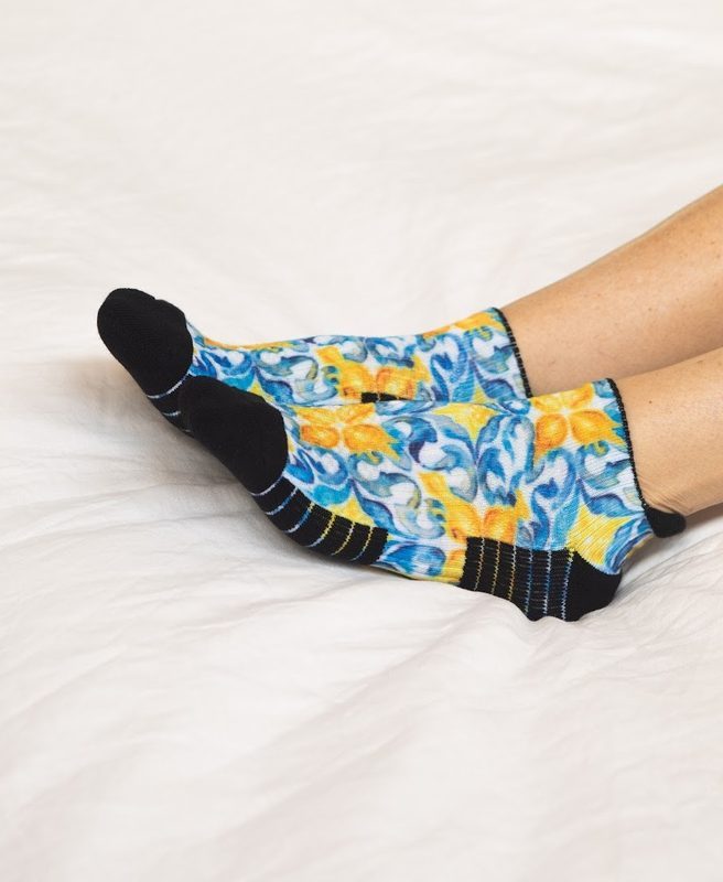 Resting on a white bed in blue and yellow lemon ankle compression socks