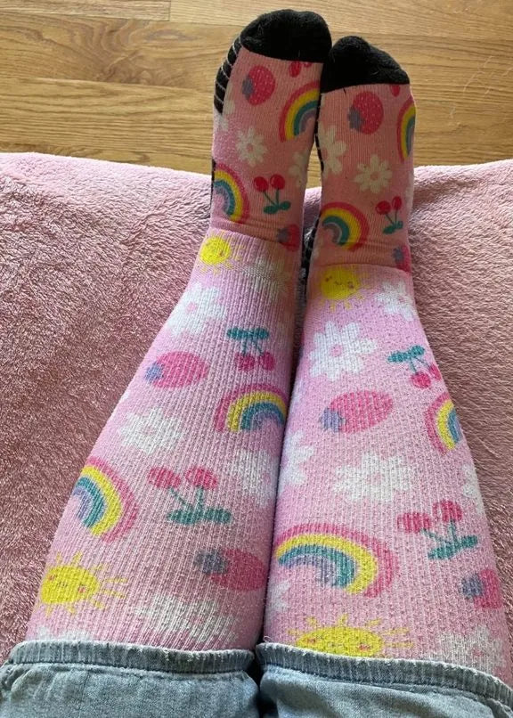 Pink rainbow and cherry EasyStretch™ socks worn with legs up on a blanket