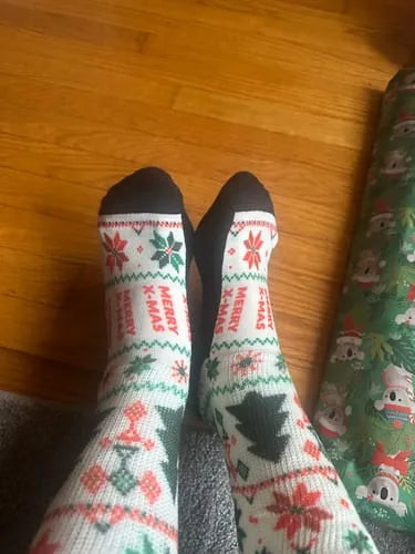 White, green and red holiday-pattern EasyStretch™ socks worn standing on a wood floor